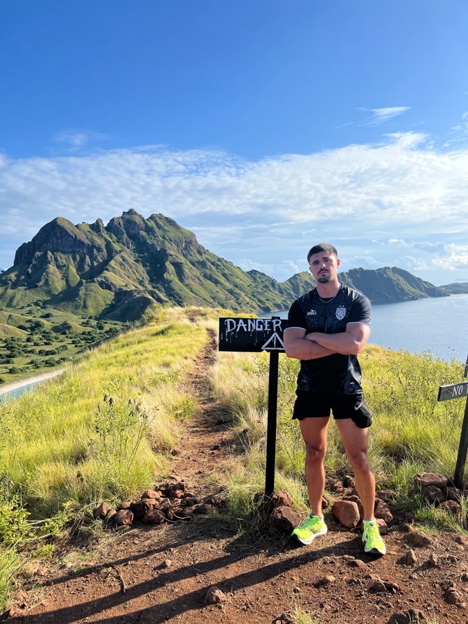 Robbie on a hike in Indonesia next to a danger sign